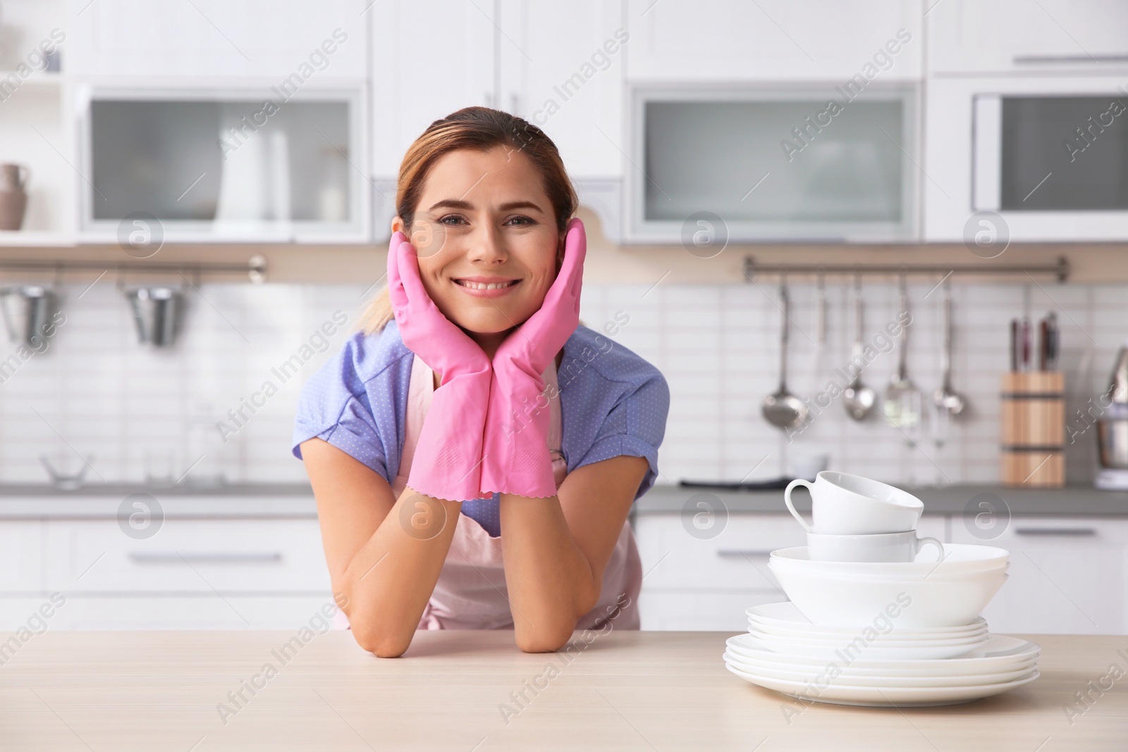 Photo of Woman in rubber gloves with clean dishes and cups in kitchen