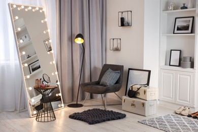 Photo of Makeup room. Stylish mirror with light bulbs, beauty products on table and armchair indoors