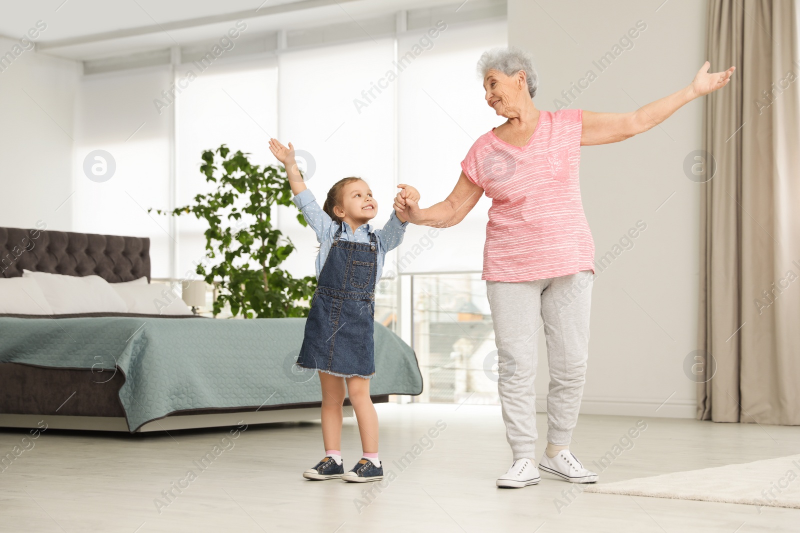 Photo of Cute girl and her grandmother dancing at home