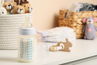Photo of Feeding bottle with milk and other baby accessories on white table near beige wall. Space for text