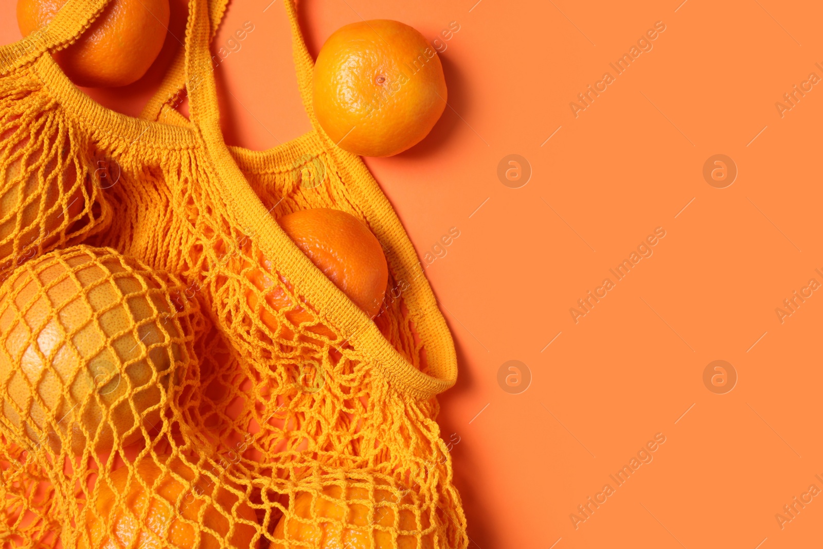 Photo of Net bag with citrus fruits on coral background, flat lay. Space for text