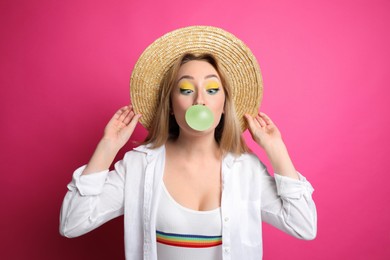 Fashionable young woman with bright makeup blowing bubblegum on pink background