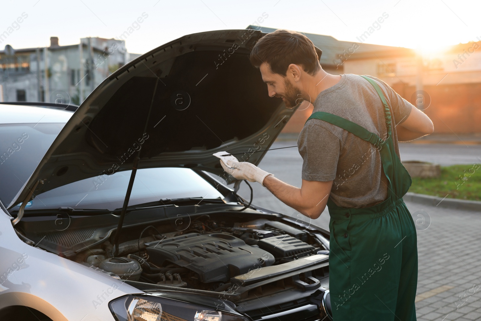 Photo of Worker checking motor oil level with dipstick outdoors