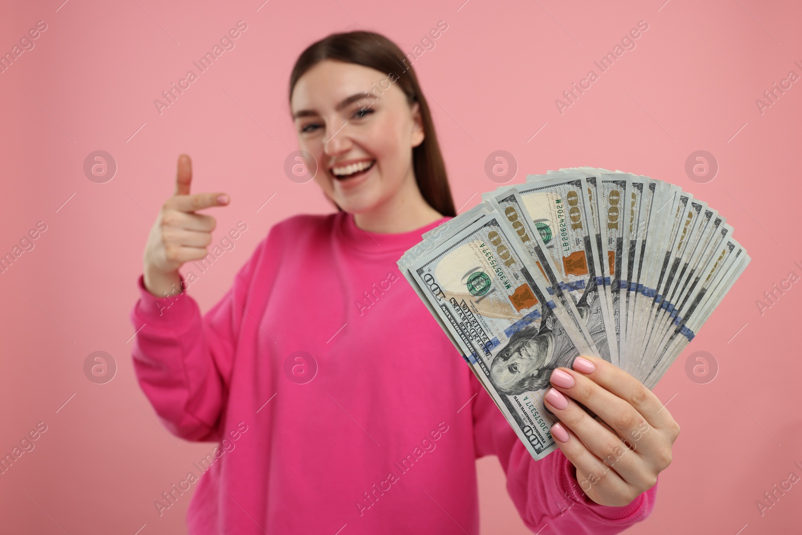 Photo of Happy woman pointing at dollar banknotes on pink background, selective focus