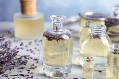 Photo of Bottles with natural herbal oil and lavender flowers on color table, closeup