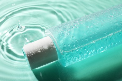 Photo of Bottle of micellar water in liquid on turquoise background