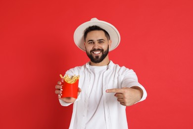 Young man with French fries on red background