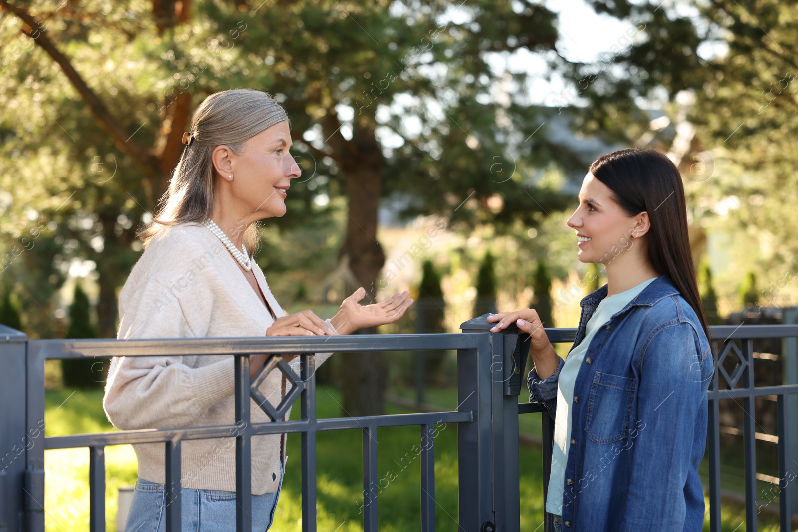 Photo of Friendly relationship with neighbours. Happy women talking near fence outdoors