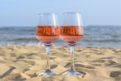 Glasses of tasty rose wine on sand near sea