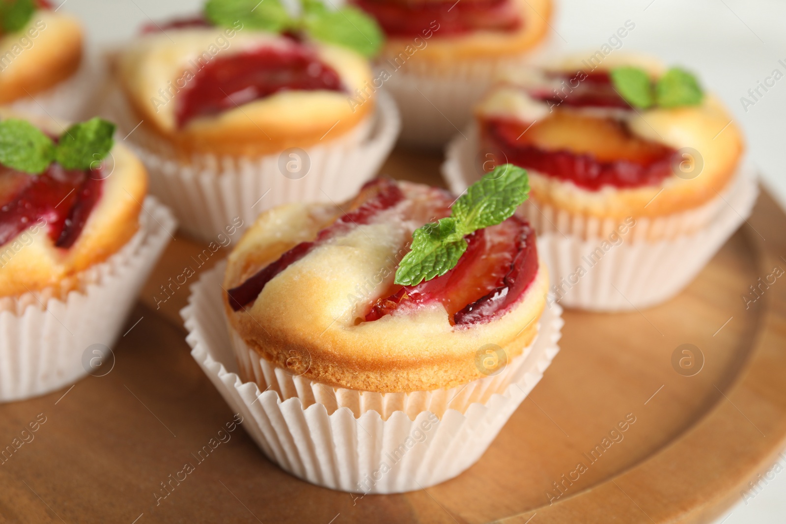 Photo of Delicious cupcakes with plums on wooden tray, closeup