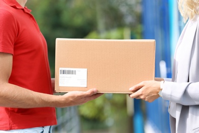 Photo of Young woman receiving parcel from courier outdoors