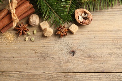 Different aromatic spices and fir branches on wooden table, flat lay. Space for text