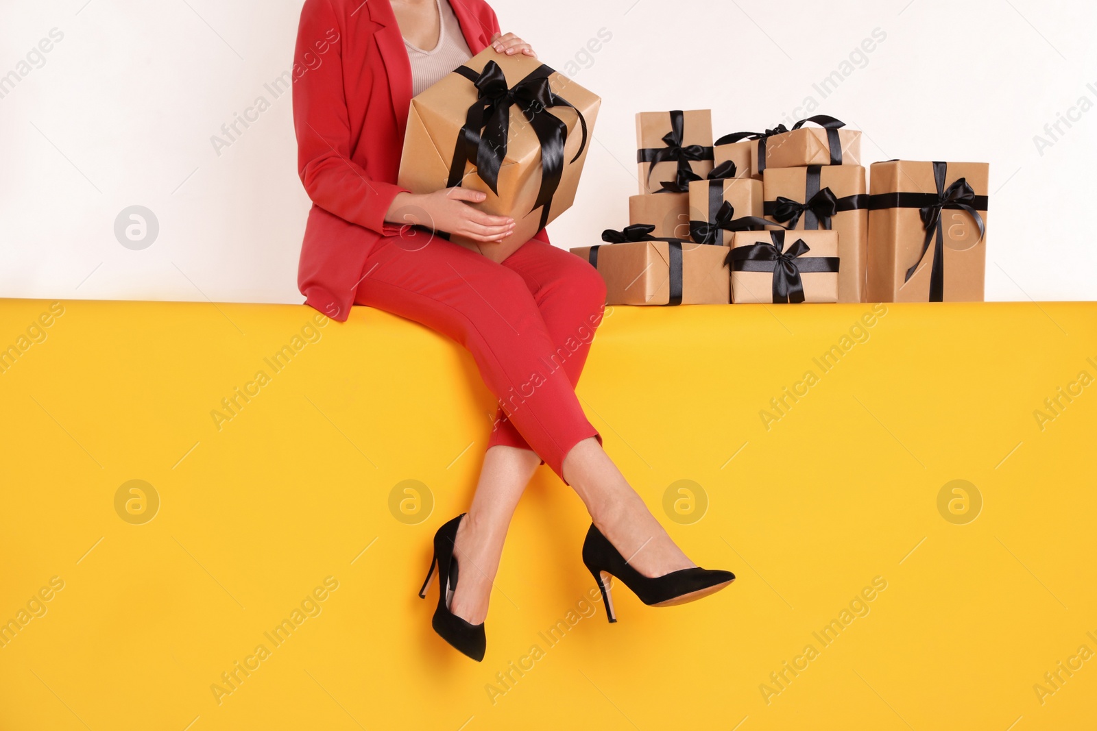 Photo of Woman with gift boxes sitting on yellow background, closeup. Black Friday