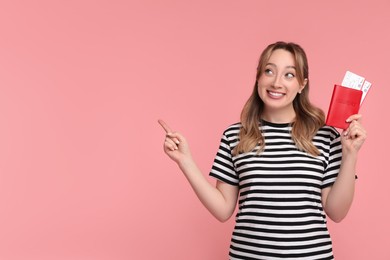Photo of Happy young woman with passport and ticket pointing at something on pink background, space for text