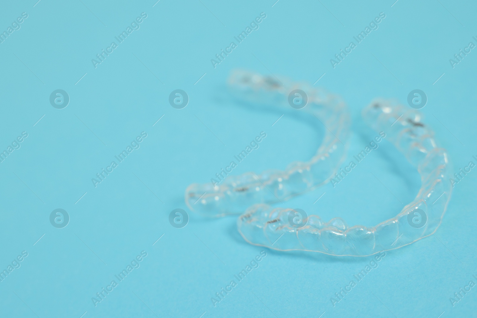 Photo of Transparent dental aligners on light blue background, closeup. Space for text