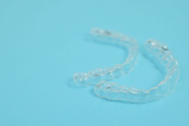 Photo of Transparent dental aligners on light blue background, closeup. Space for text