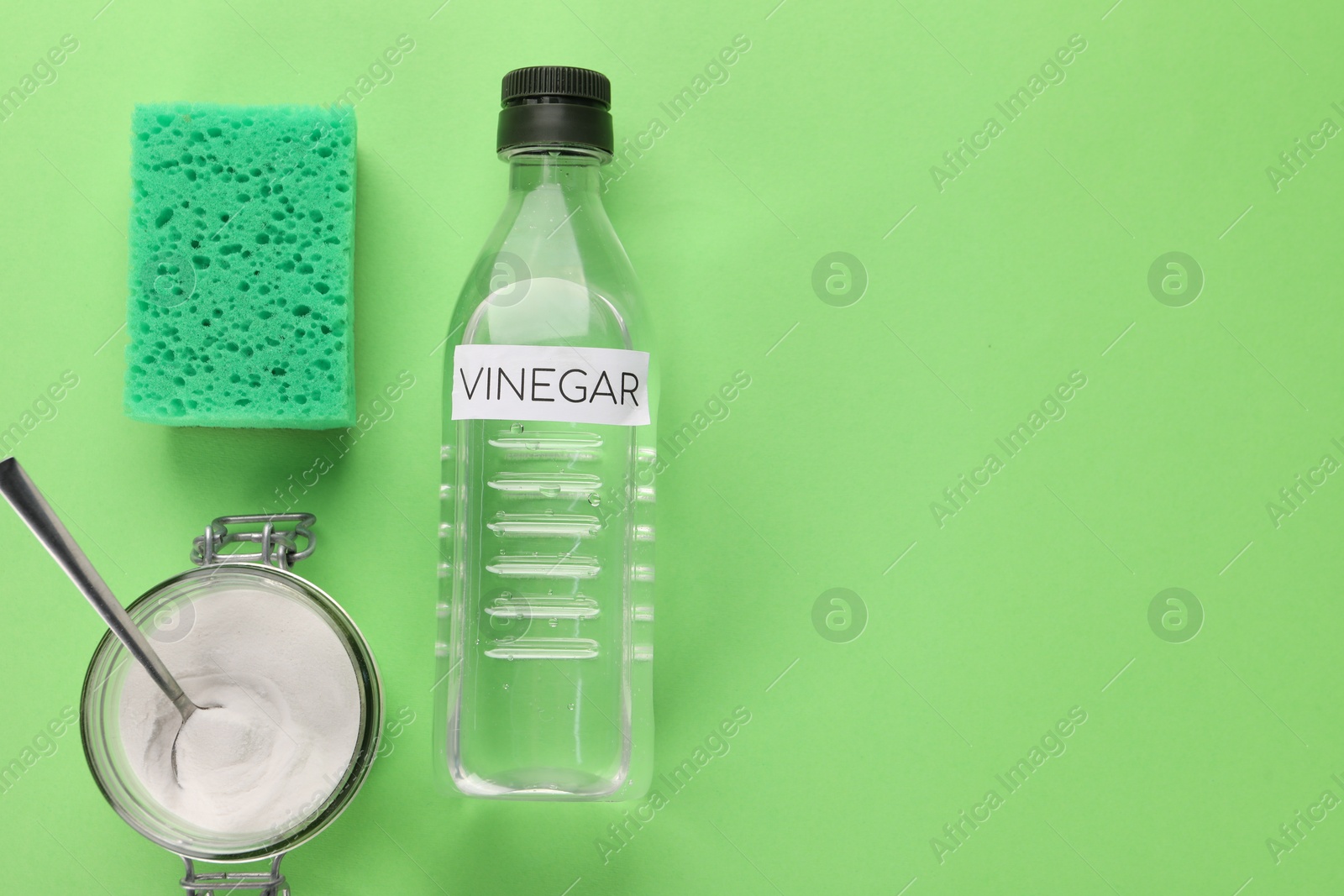 Photo of Eco friendly natural cleaners. Vinegar in bottle, sponge and jar of soda on green background, flat lay. Space for text