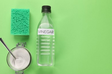 Photo of Eco friendly natural cleaners. Vinegar in bottle, sponge and jar of soda on green background, flat lay. Space for text