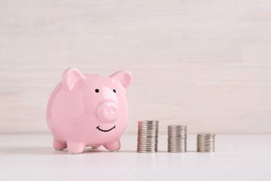 Photo of Financial savings. Piggy bank and stacked coins on white wooden table