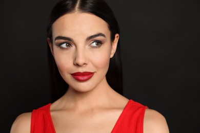 Photo of Portrait of young woman wearing beautiful red lipstick on black background