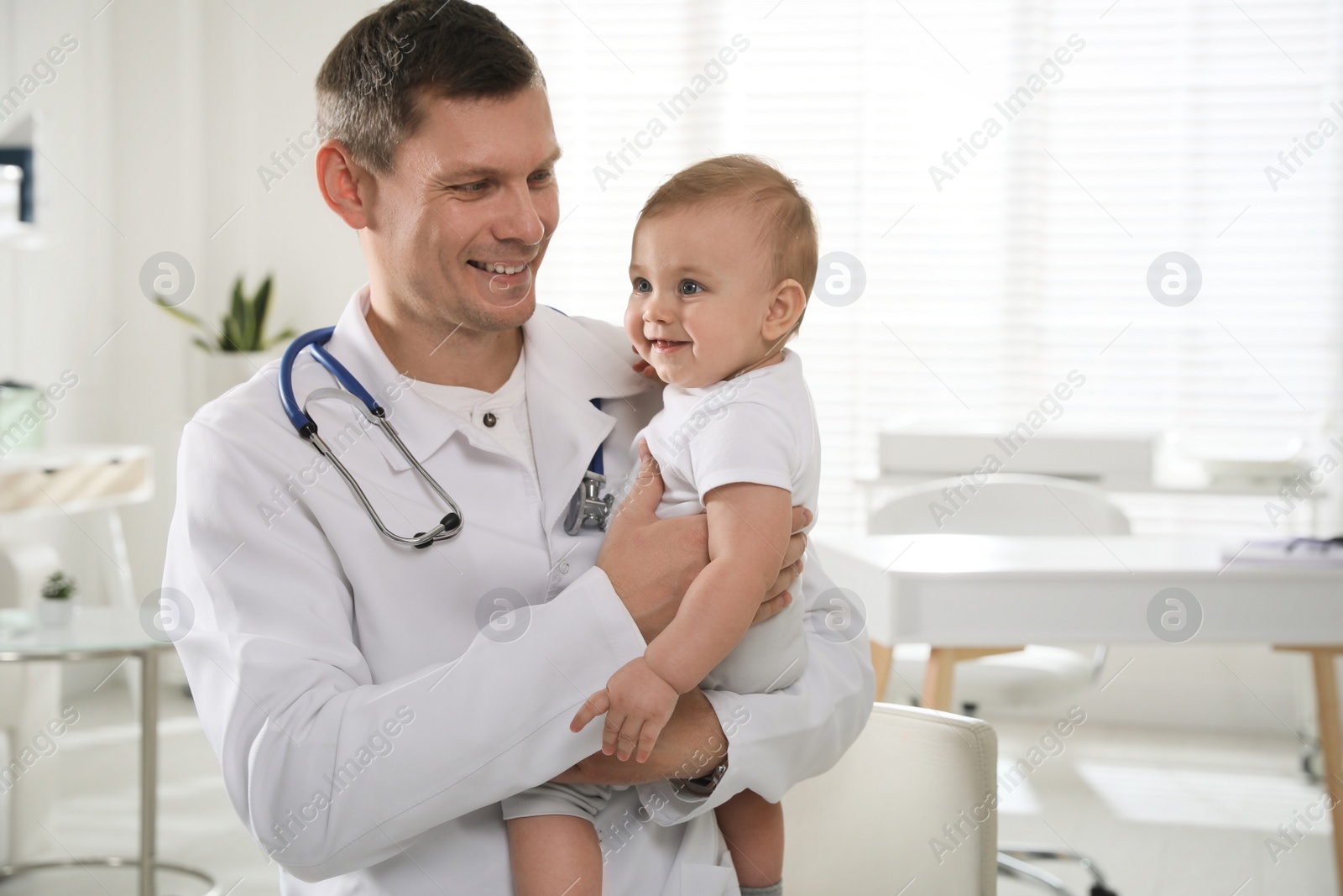 Photo of Pediatrician with cute little baby in clinic. Space for text