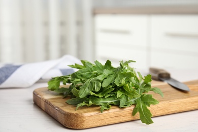 Photo of Fresh arugula, cutting board and knife on table indoors. Space for text