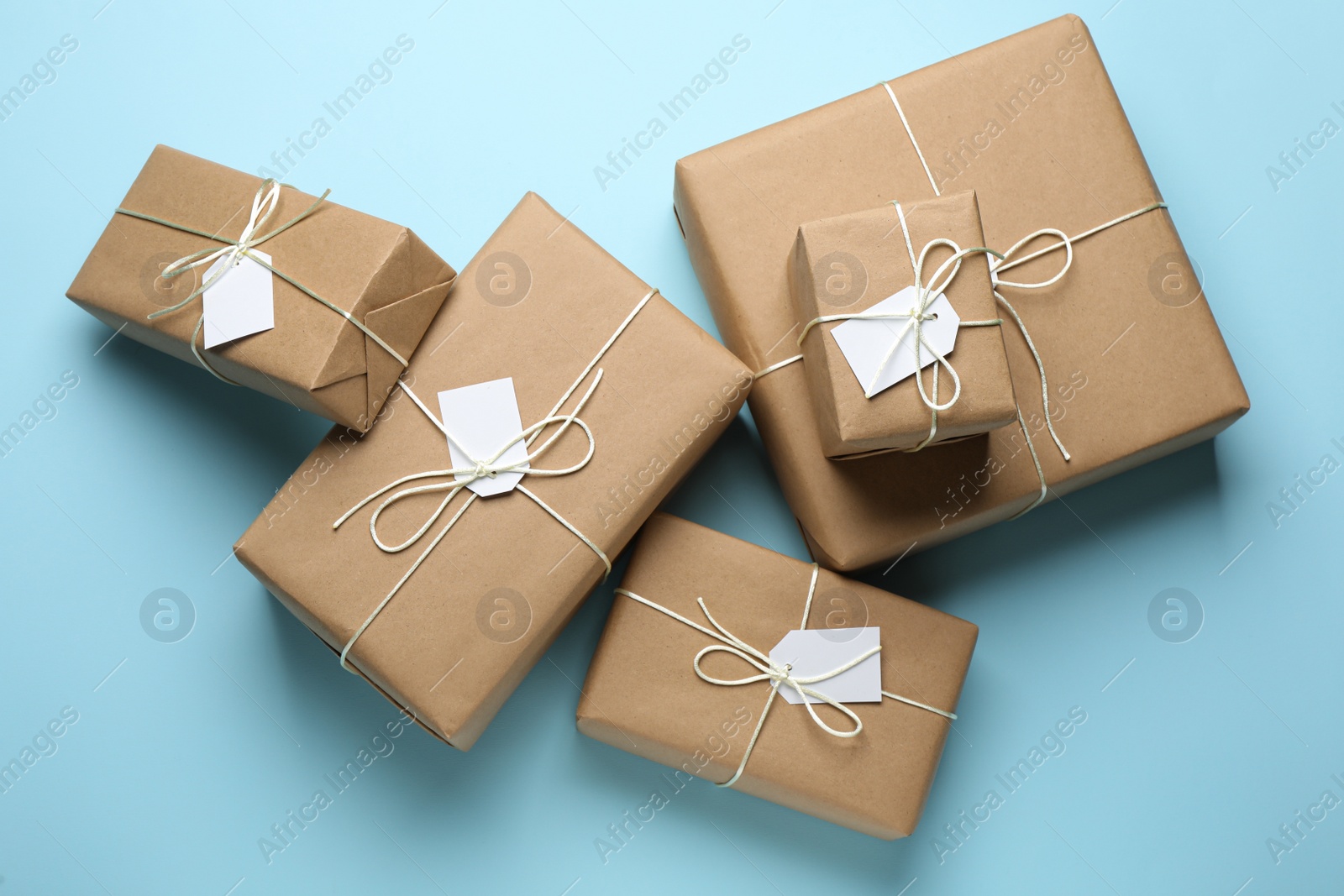 Photo of Parcels wrapped in kraft paper with tags on light blue background, flat lay