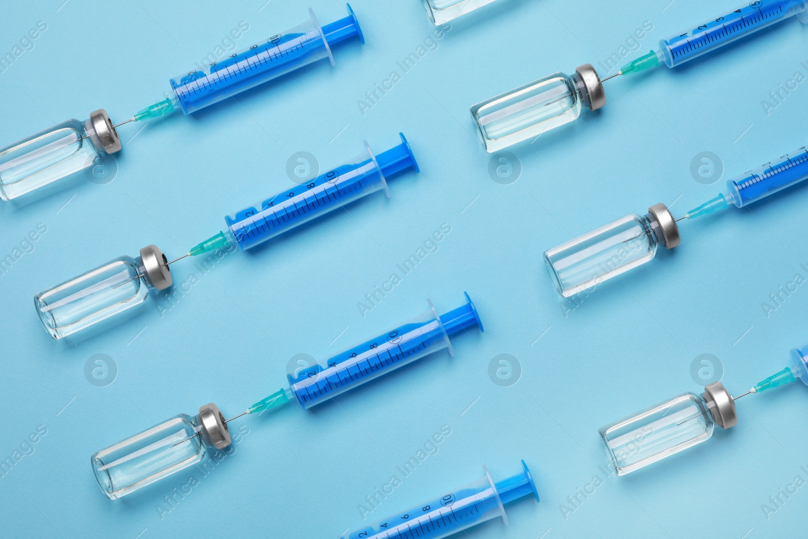 Photo of Disposable syringes with needles and vials on light blue background, flat lay