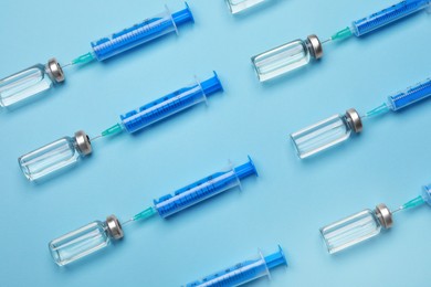 Disposable syringes with needles and vials on light blue background, flat lay