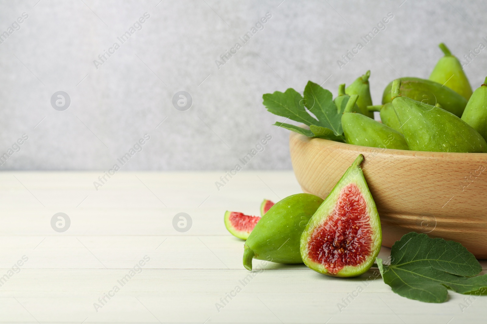 Photo of Cut and whole fresh green figs on white wooden table near grey wall, space for text