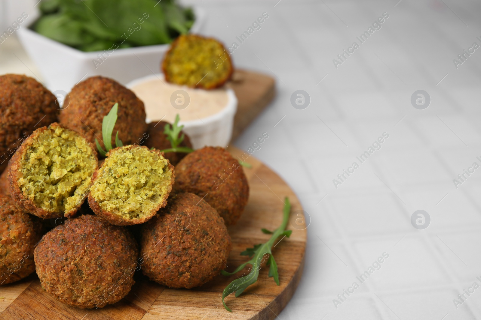 Photo of Delicious falafel balls and arugula on white tiled table, space for text