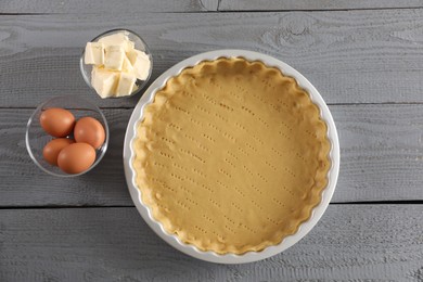 Photo of Making quiche. Baking dish with fresh dough and ingredients on grey wooden table, flat lay