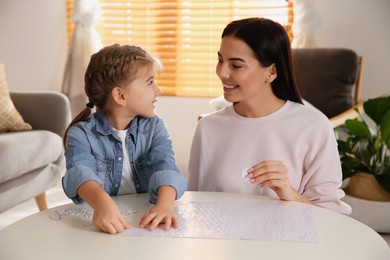 Happy mother and her daughter playing with puzzles at home