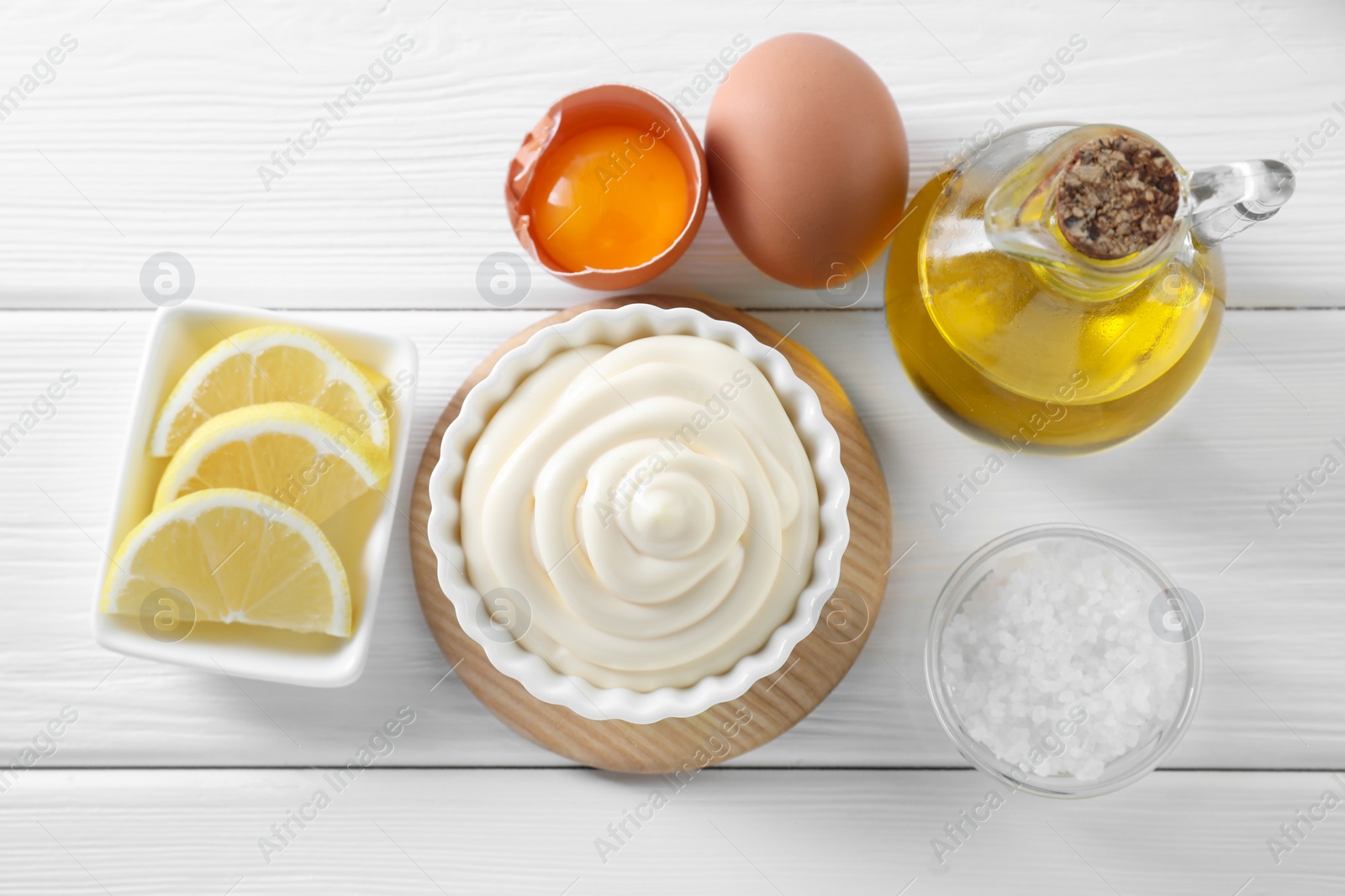 Photo of Fresh mayonnaise sauce in bowl and ingredients on white wooden table, flat lay