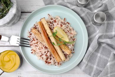 Plate with baked salsify roots, lemon, rice and fork on white wooden table, flat lay