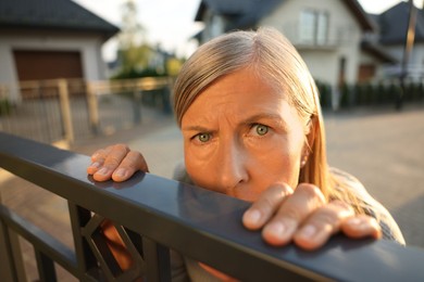 Photo of Concept of private life. Curious senior woman spying on neighbours over fence outdoors, closeup