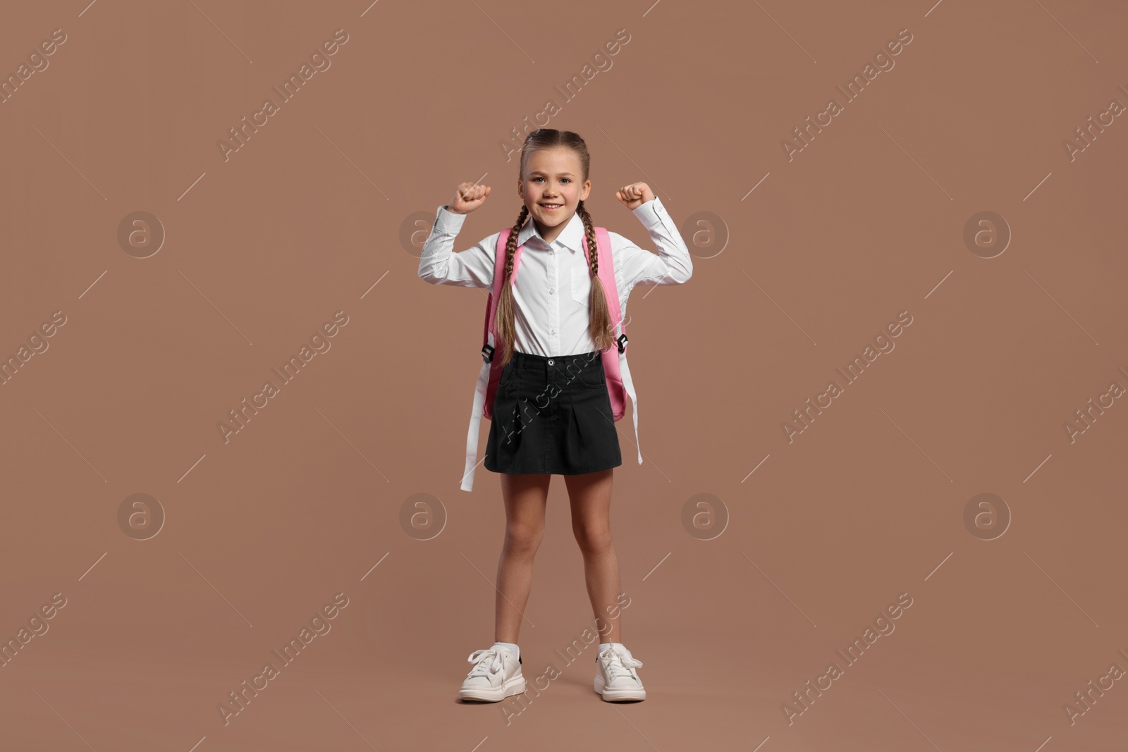 Photo of Happy schoolgirl with backpack on brown background