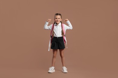 Photo of Happy schoolgirl with backpack on brown background