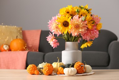 Photo of Autumn mood. Beautiful bouquet with bright flowers and small pumpkins on wooden table in room, space for text