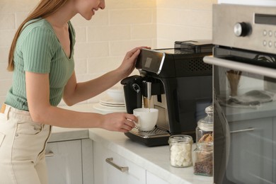 Photo of Young woman preparing fresh aromatic coffee with modern machine in kitchen, closeup