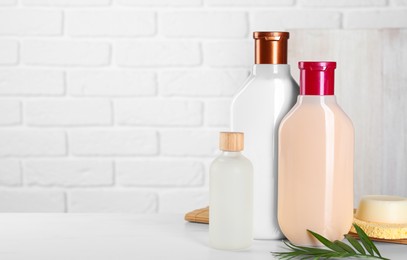 Photo of Different bottles of shampoo and green leaf on white table, space for text