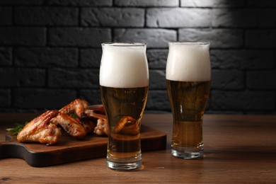 Glasses with beer and delicious baked chicken wings on wooden table