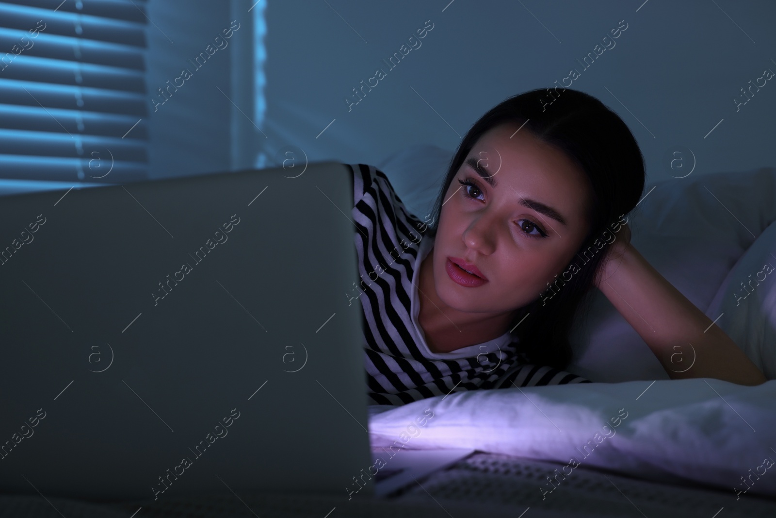 Photo of Young woman using laptop on bed at night. Internet addiction