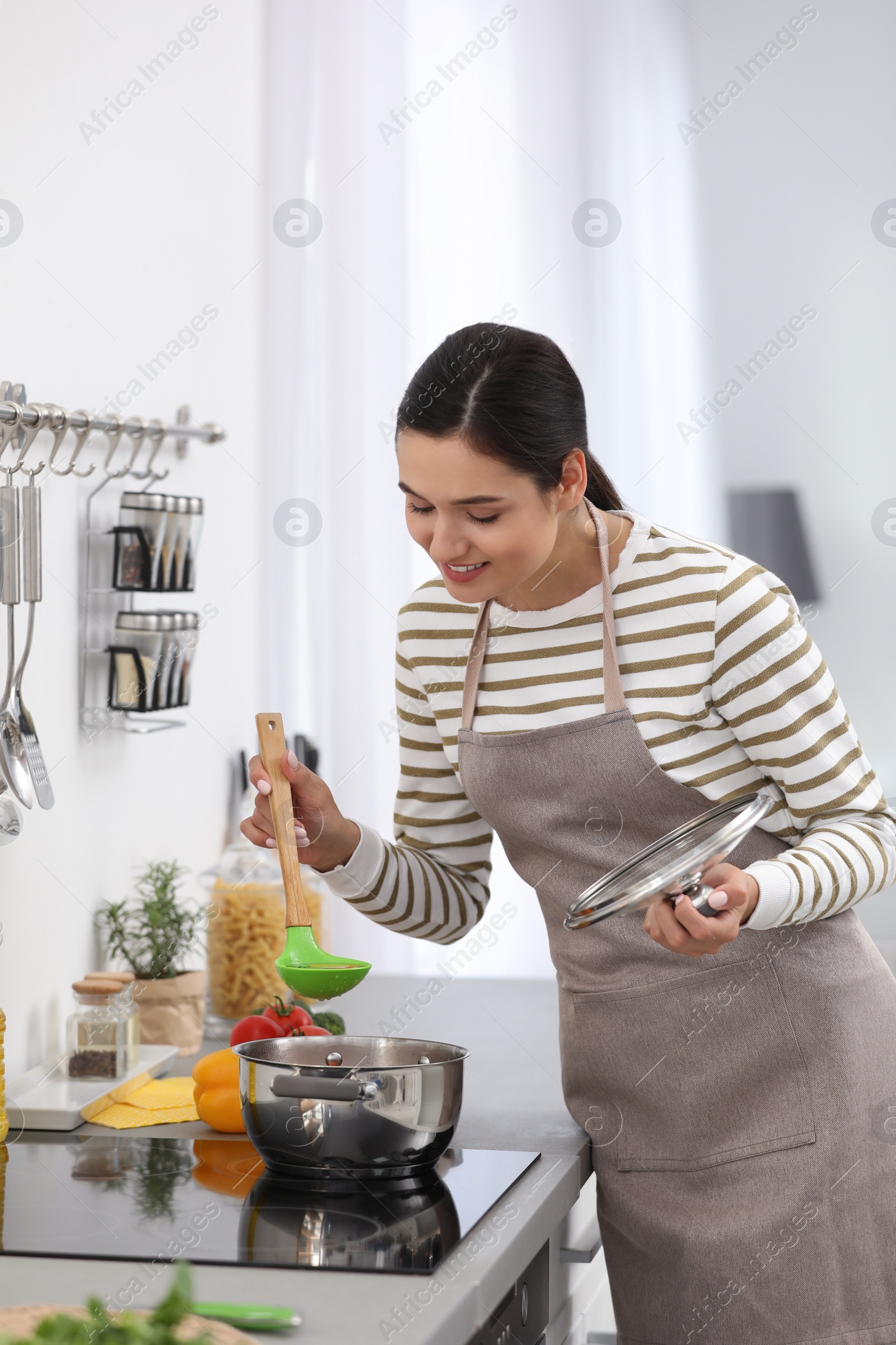 Photo of Young woman cooking tasty soup in kitchen