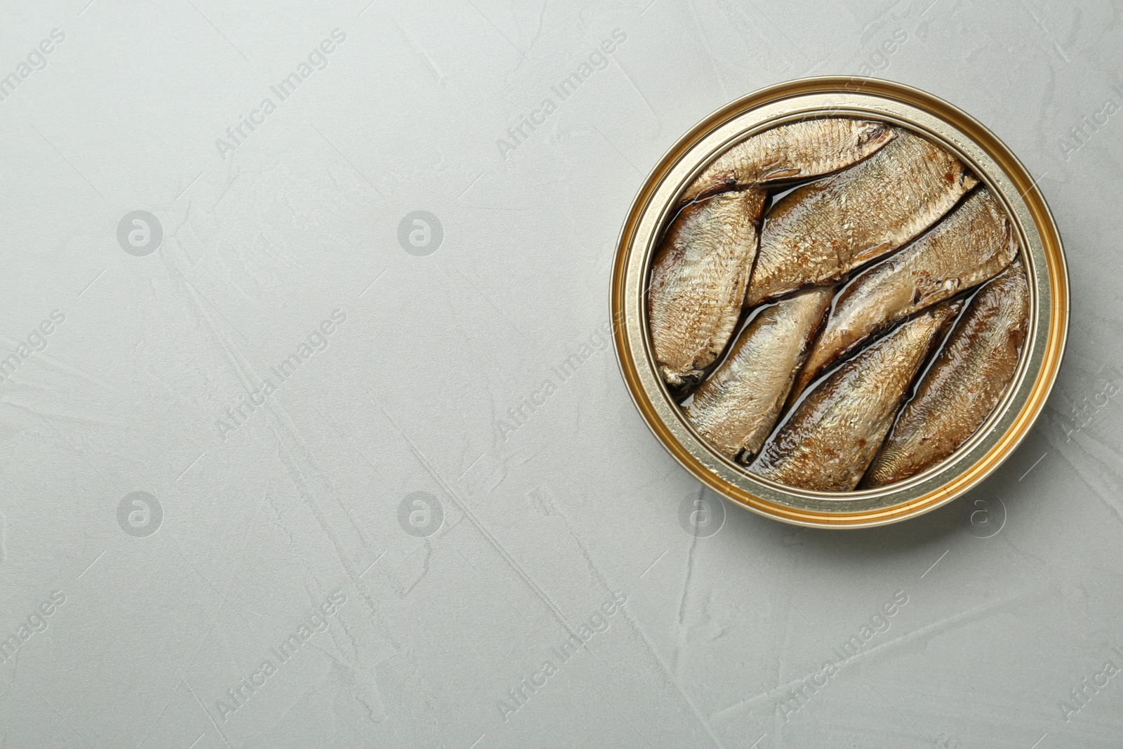 Photo of Open tin can of sprats on light grey table, top view. Space for text