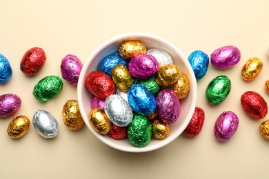 Chocolate eggs wrapped in colorful foil on beige background, flat lay