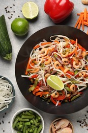 Shrimp stir fry with noodles and vegetables in wok surrounded by ingredients on grey table, flat lay