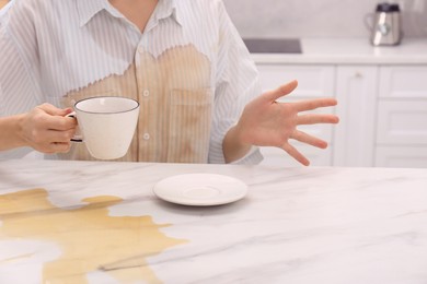 Photo of Woman with spilled coffee over her shirt at marble table in kitchen, closeup