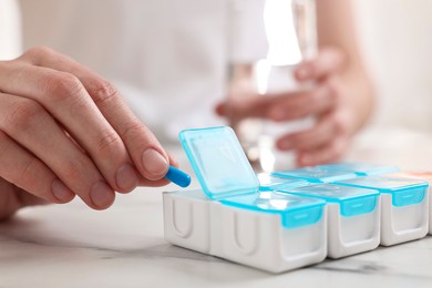 Photo of Woman with pills and organizer at white marble table, closeup