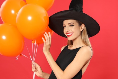 Photo of Beautiful woman wearing witch costume with balloons for Halloween party on red background